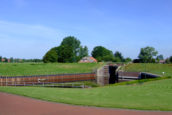 Sieltoranlage in grüner Landschaft bei Petkum, von Wassergraben und Wiesen umgeben.