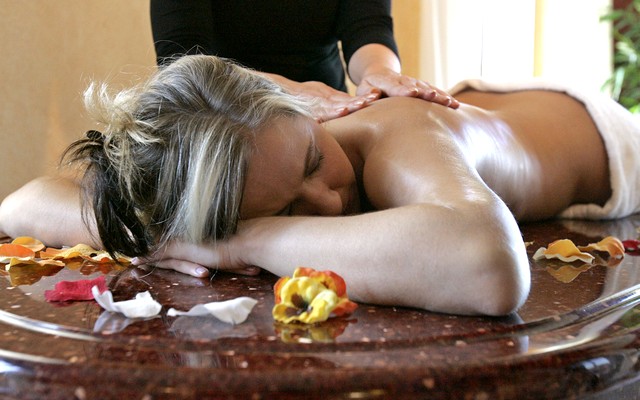 Frau genießt eine Wellnessmassage, Rosenblätter und Kerzen für Entspannung.