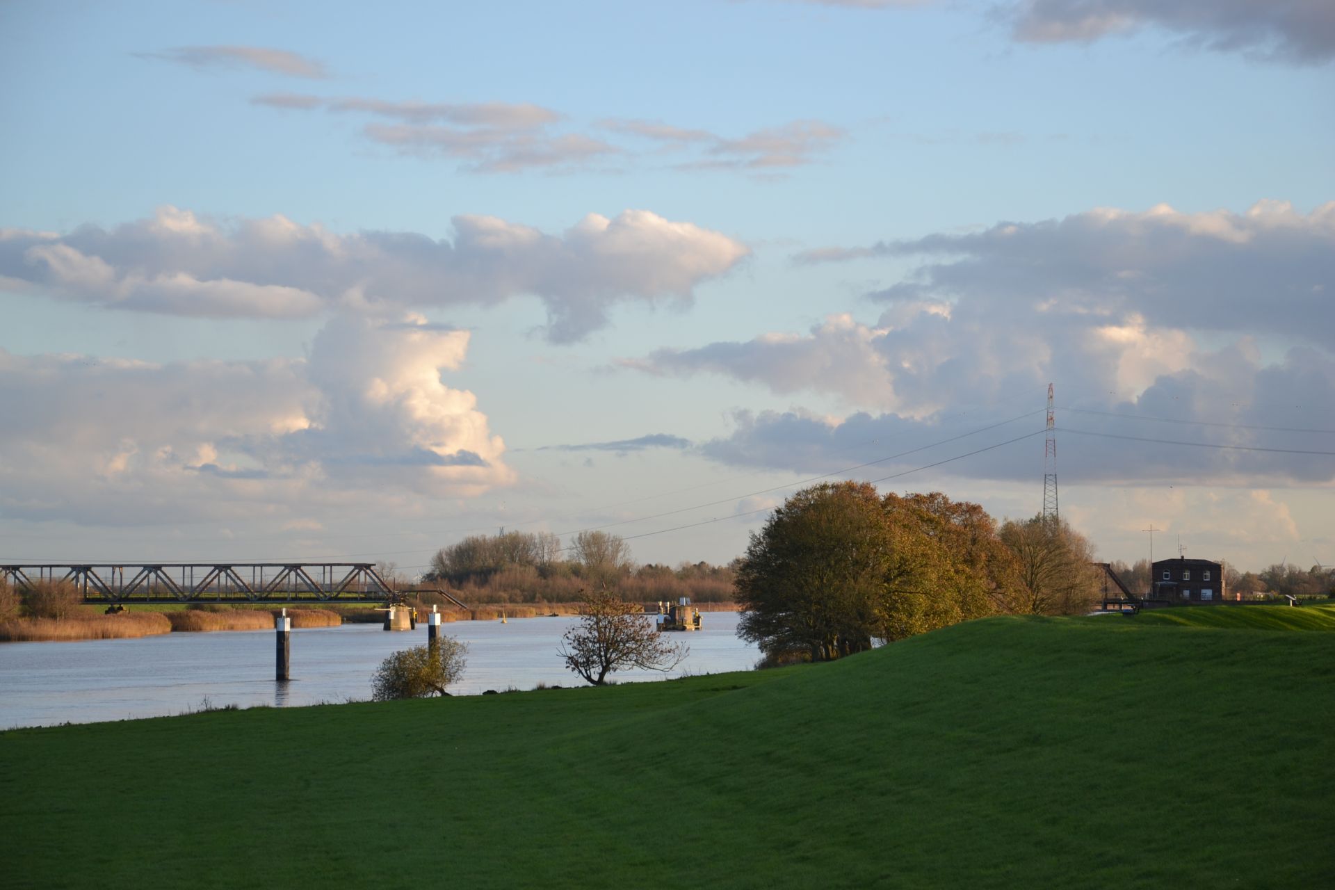 Foto: Naturkulisse, welche Deich, Wasser und ein Eisenbahnbrücke in der Ferne miteinander vereint.